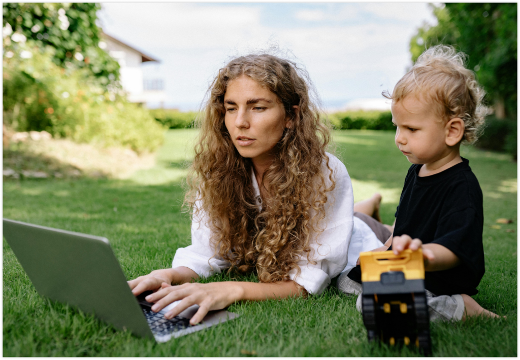 A woman and small child lie on the grass, looking at a laptop